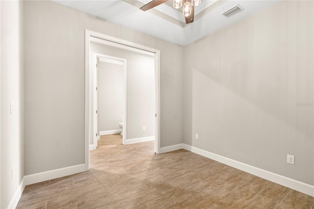 spare room featuring ceiling fan, light wood-type flooring, and a tray ceiling