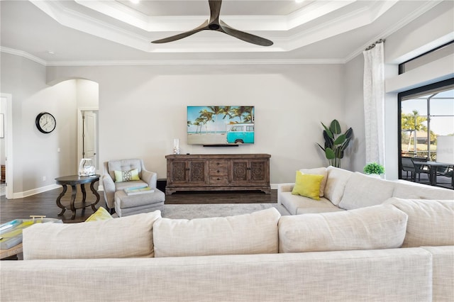 living area featuring crown molding, a tray ceiling, arched walkways, a ceiling fan, and wood finished floors