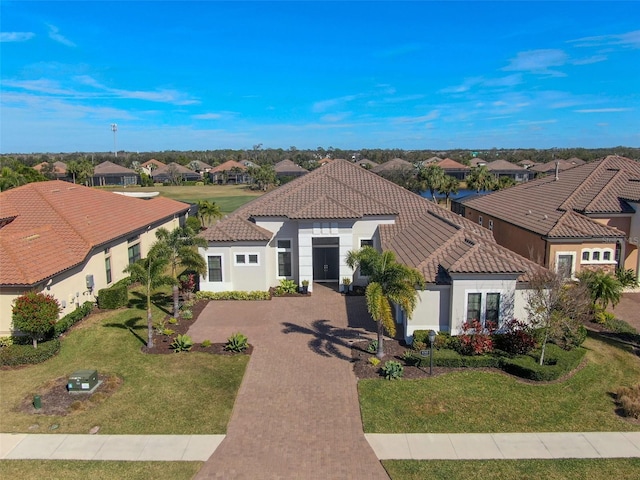 mediterranean / spanish house featuring a tiled roof, stucco siding, a residential view, and a front lawn