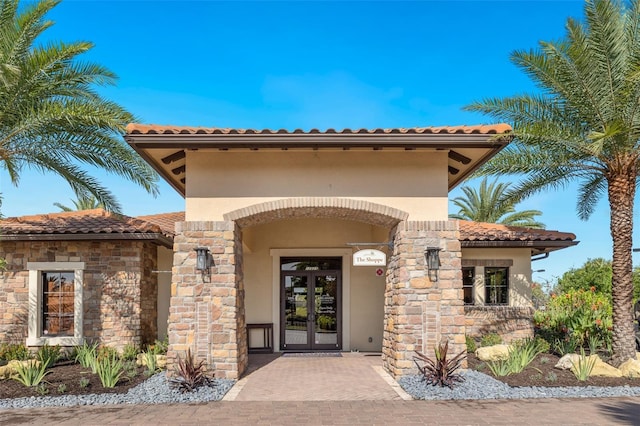 property entrance with french doors, stone siding, stucco siding, and a tile roof