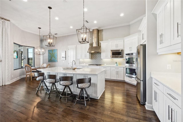 kitchen with crown molding, an inviting chandelier, wall chimney range hood, white cabinetry, and stainless steel appliances