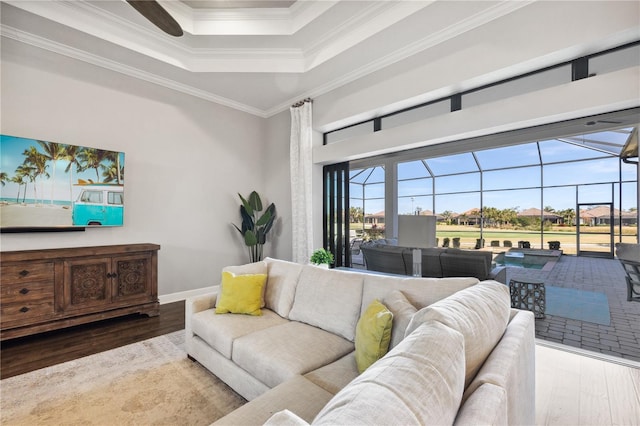 living area with crown molding, a sunroom, a tray ceiling, wood finished floors, and baseboards