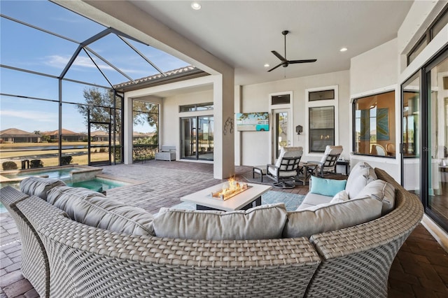 view of patio / terrace with a pool with connected hot tub, a ceiling fan, a lanai, and an outdoor living space with a fire pit