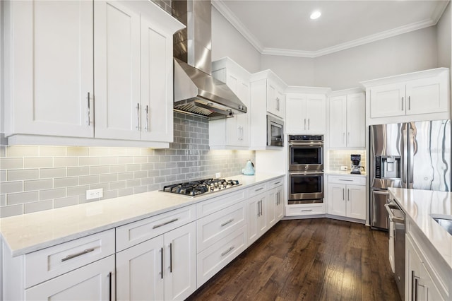 kitchen featuring wall chimney range hood, white cabinetry, crown molding, dark wood finished floors, and stainless steel appliances