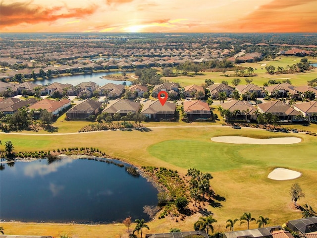 aerial view at dusk with a water view, golf course view, and a residential view
