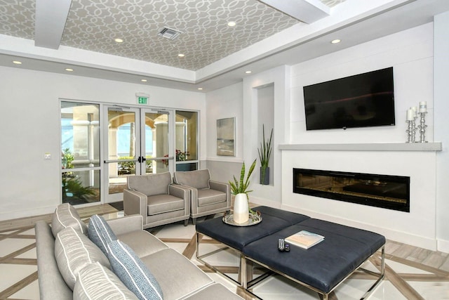 living room featuring visible vents, a raised ceiling, a glass covered fireplace, french doors, and recessed lighting