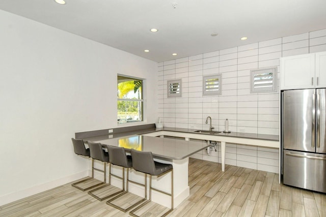 kitchen featuring stainless steel refrigerator, a peninsula, light wood-type flooring, white cabinetry, and a sink