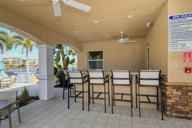 view of patio featuring a water view, outdoor dry bar, and a ceiling fan