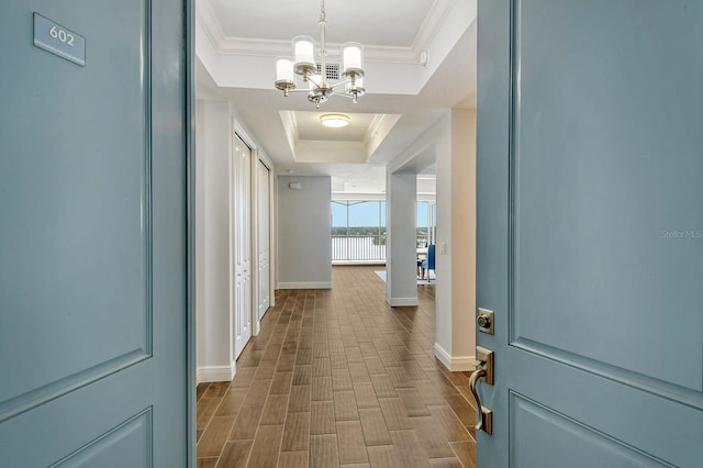 hallway featuring baseboards, a tray ceiling, dark wood-type flooring, and crown molding