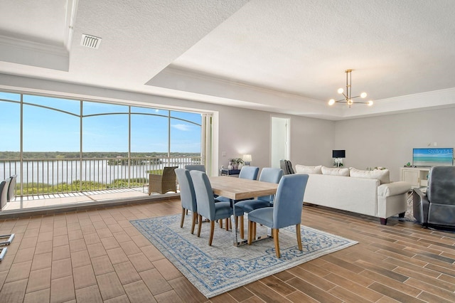 dining area with a chandelier, wood tiled floor, a raised ceiling, and a water view