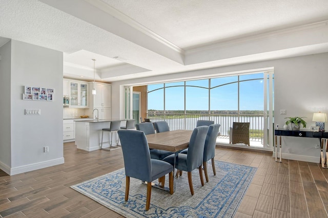 dining room with wood finish floors, a raised ceiling, a water view, a textured ceiling, and baseboards