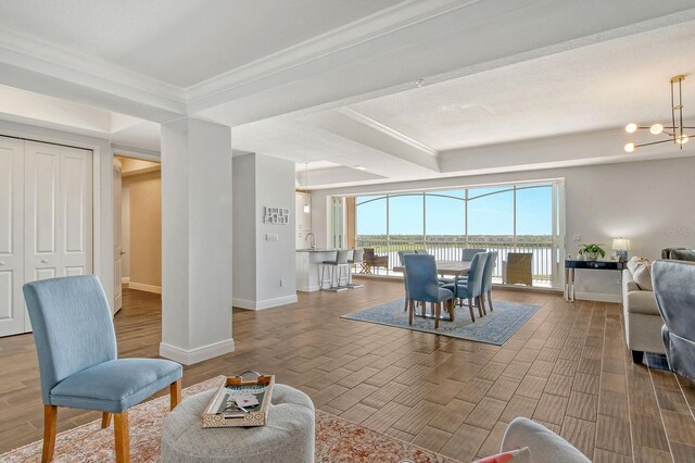 living area featuring an inviting chandelier, a tray ceiling, crown molding, and wood finish floors