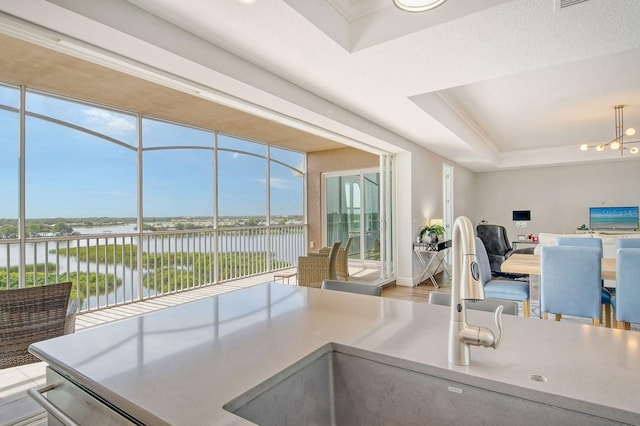 kitchen featuring a notable chandelier, a water view, a sink, open floor plan, and a tray ceiling