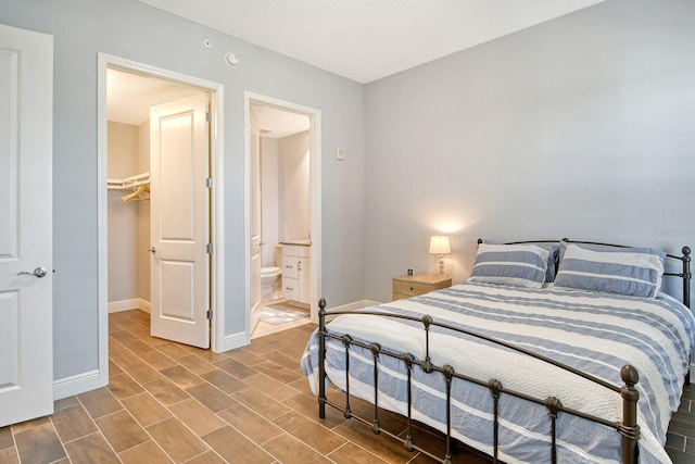 bedroom featuring ensuite bathroom, wood finish floors, a walk in closet, and baseboards