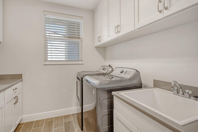 laundry area with washing machine and dryer, a sink, baseboards, cabinet space, and wood tiled floor