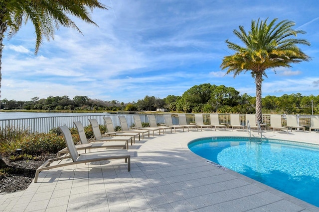 pool featuring a water view, a patio area, and fence