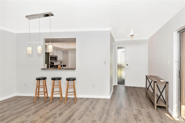 kitchen with light wood-type flooring, ornamental molding, kitchen peninsula, pendant lighting, and white cabinets