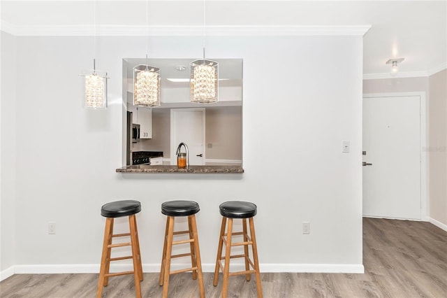 kitchen with sink, crown molding, a breakfast bar area, wood-type flooring, and kitchen peninsula