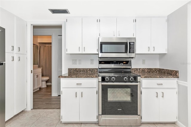 kitchen featuring white cabinetry, light tile patterned floors, dark stone counters, and black gas stove