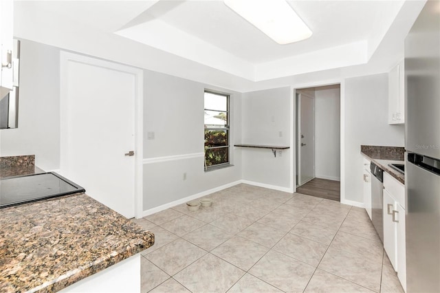 kitchen with light tile patterned flooring, stainless steel dishwasher, a tray ceiling, dark stone counters, and white cabinets