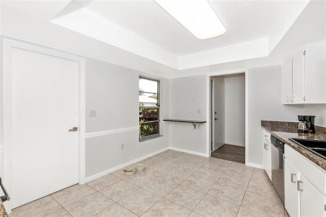 kitchen with light tile patterned floors, dishwasher, a tray ceiling, white cabinets, and dark stone counters