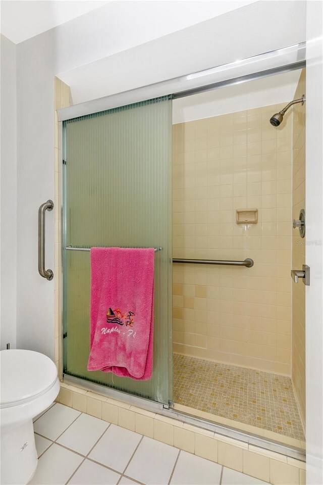 bathroom with tile patterned floors, toilet, and a shower with door