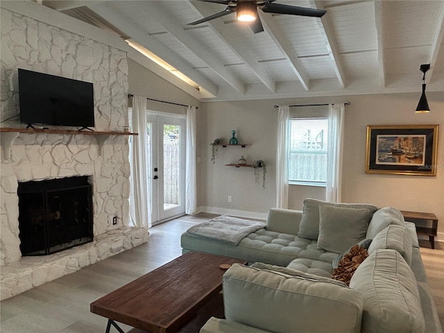 living room with a stone fireplace, vaulted ceiling with beams, a wealth of natural light, and light hardwood / wood-style floors