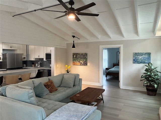 living room with vaulted ceiling with beams, light hardwood / wood-style flooring, sink, and ceiling fan