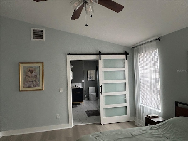 bedroom with multiple windows, a barn door, lofted ceiling, and light wood-type flooring