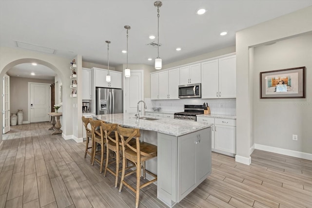 kitchen featuring pendant lighting, white cabinetry, appliances with stainless steel finishes, and a center island with sink