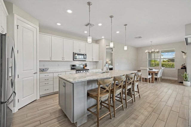 kitchen featuring an island with sink, white cabinetry, a kitchen breakfast bar, hanging light fixtures, and stainless steel appliances