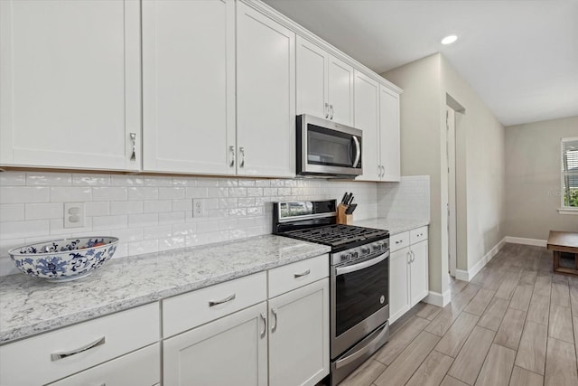 kitchen with light hardwood / wood-style flooring, white cabinetry, backsplash, stainless steel appliances, and light stone countertops