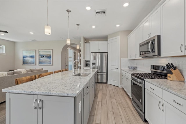 kitchen with white cabinetry, appliances with stainless steel finishes, sink, and a center island with sink