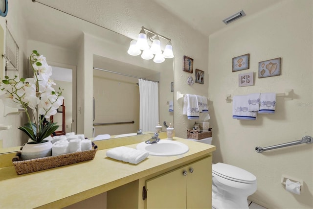 bathroom featuring vanity, toilet, a textured wall, and visible vents