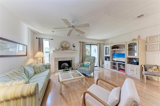 living room with a tile fireplace, ceiling fan, a textured ceiling, and light hardwood / wood-style flooring