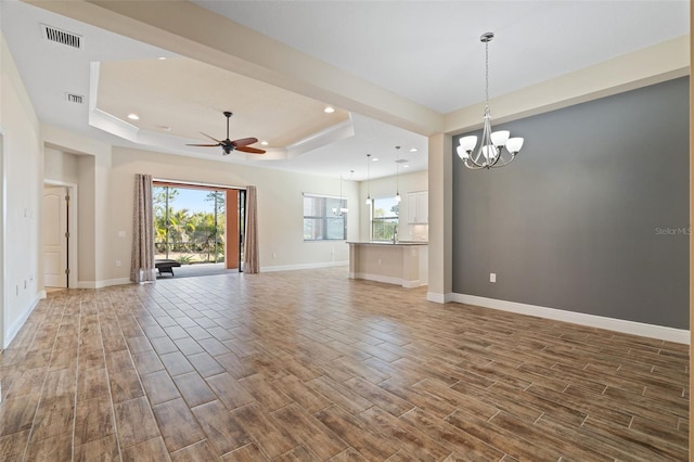 unfurnished living room with hardwood / wood-style flooring, ceiling fan with notable chandelier, and a raised ceiling