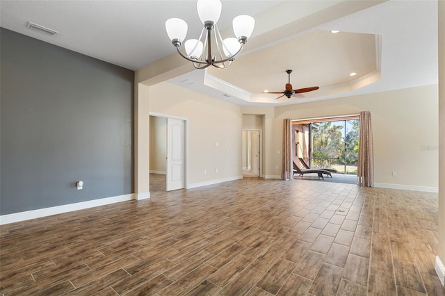 interior space featuring a tray ceiling, wood-type flooring, and ceiling fan with notable chandelier