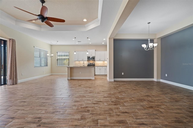 unfurnished living room with sink, a tray ceiling, and ceiling fan with notable chandelier