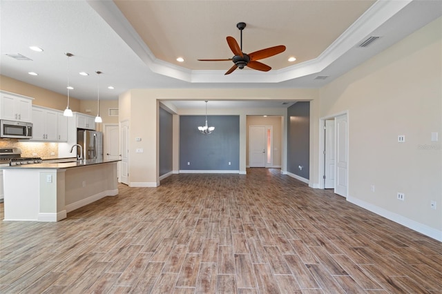 unfurnished living room featuring ceiling fan with notable chandelier, a tray ceiling, light hardwood / wood-style floors, and crown molding