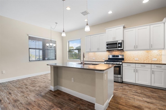 kitchen featuring white cabinetry, decorative light fixtures, a center island with sink, appliances with stainless steel finishes, and decorative backsplash