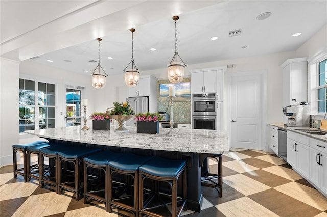 kitchen with pendant lighting, a breakfast bar, appliances with stainless steel finishes, white cabinetry, and a spacious island