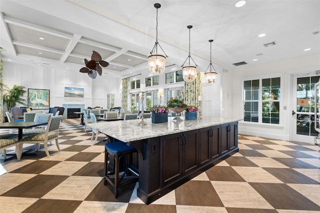 kitchen featuring coffered ceiling, light stone counters, pendant lighting, a towering ceiling, and a large island