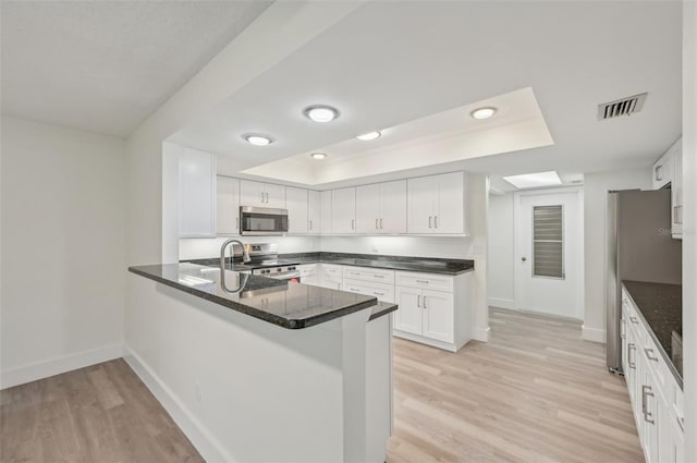 kitchen with light hardwood / wood-style flooring, stainless steel appliances, kitchen peninsula, white cabinets, and a raised ceiling