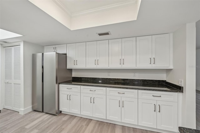 kitchen with light hardwood / wood-style flooring, stainless steel refrigerator, ornamental molding, dark stone counters, and white cabinets