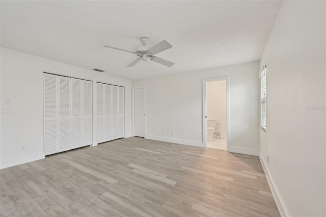 unfurnished bedroom with ceiling fan, connected bathroom, light hardwood / wood-style floors, a textured ceiling, and multiple closets