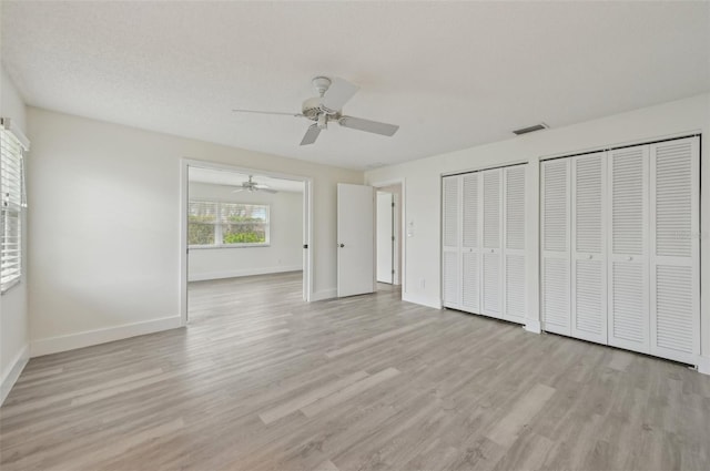 unfurnished bedroom featuring multiple closets, a textured ceiling, ceiling fan, and light hardwood / wood-style flooring