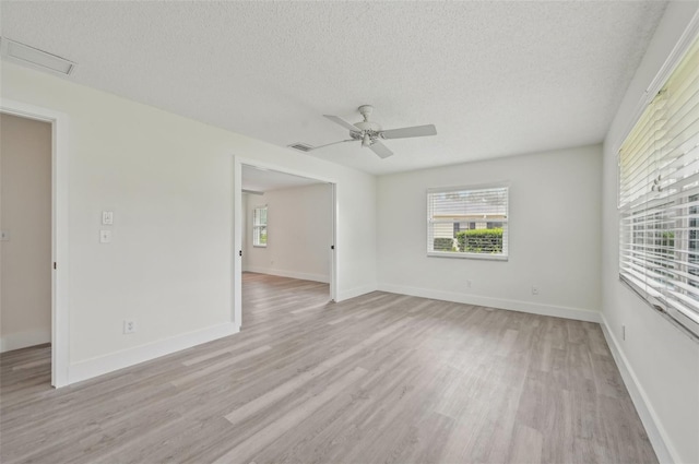 empty room featuring ceiling fan, a wealth of natural light, a textured ceiling, and light wood-type flooring