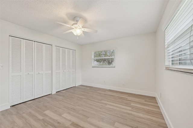 unfurnished bedroom with multiple closets, ceiling fan, a textured ceiling, and light wood-type flooring