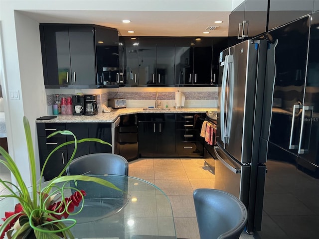 kitchen featuring light tile patterned flooring, sink, light stone counters, stainless steel fridge, and decorative backsplash