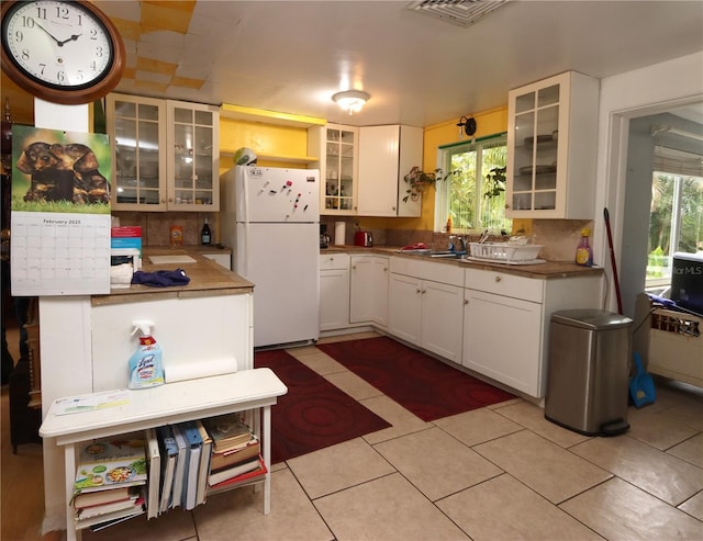 kitchen with light tile patterned flooring, sink, white cabinetry, white refrigerator, and decorative backsplash